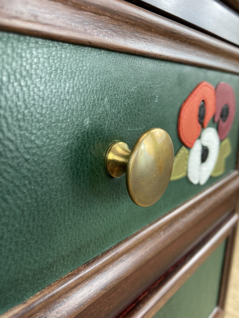 Détail d'un bouton en laiton et du cuir vert d'un tiroir